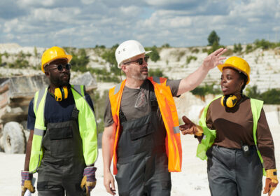 Mature foreman in workwear and hardhat pointing at part of marble quarry while talking to African American subordinates